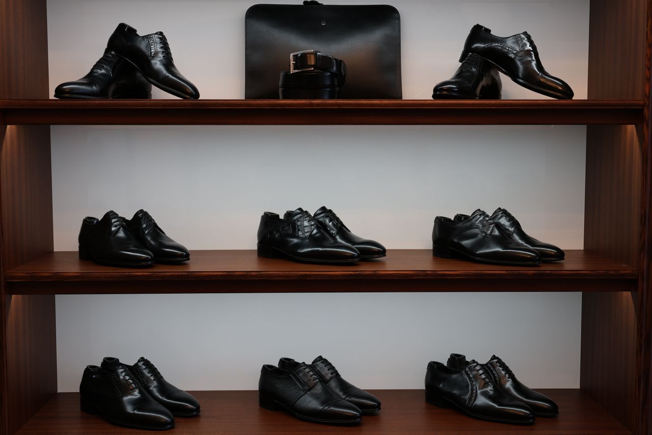 about-bg A stylish display of black leather shoes and accessories on wooden shelves in a store.