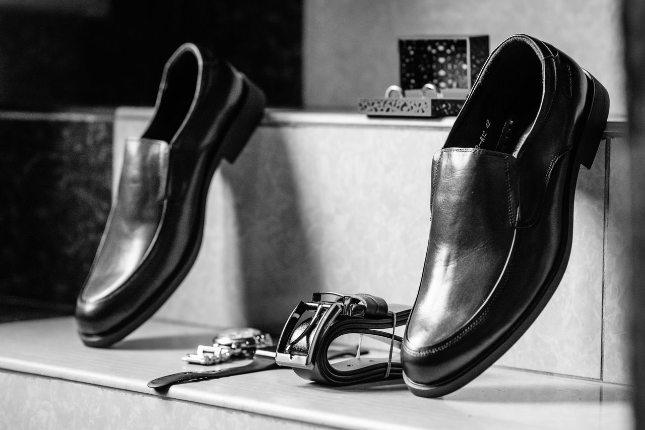 services-04 Stylish black leather formal shoes paired with accessories in a black and white setting.