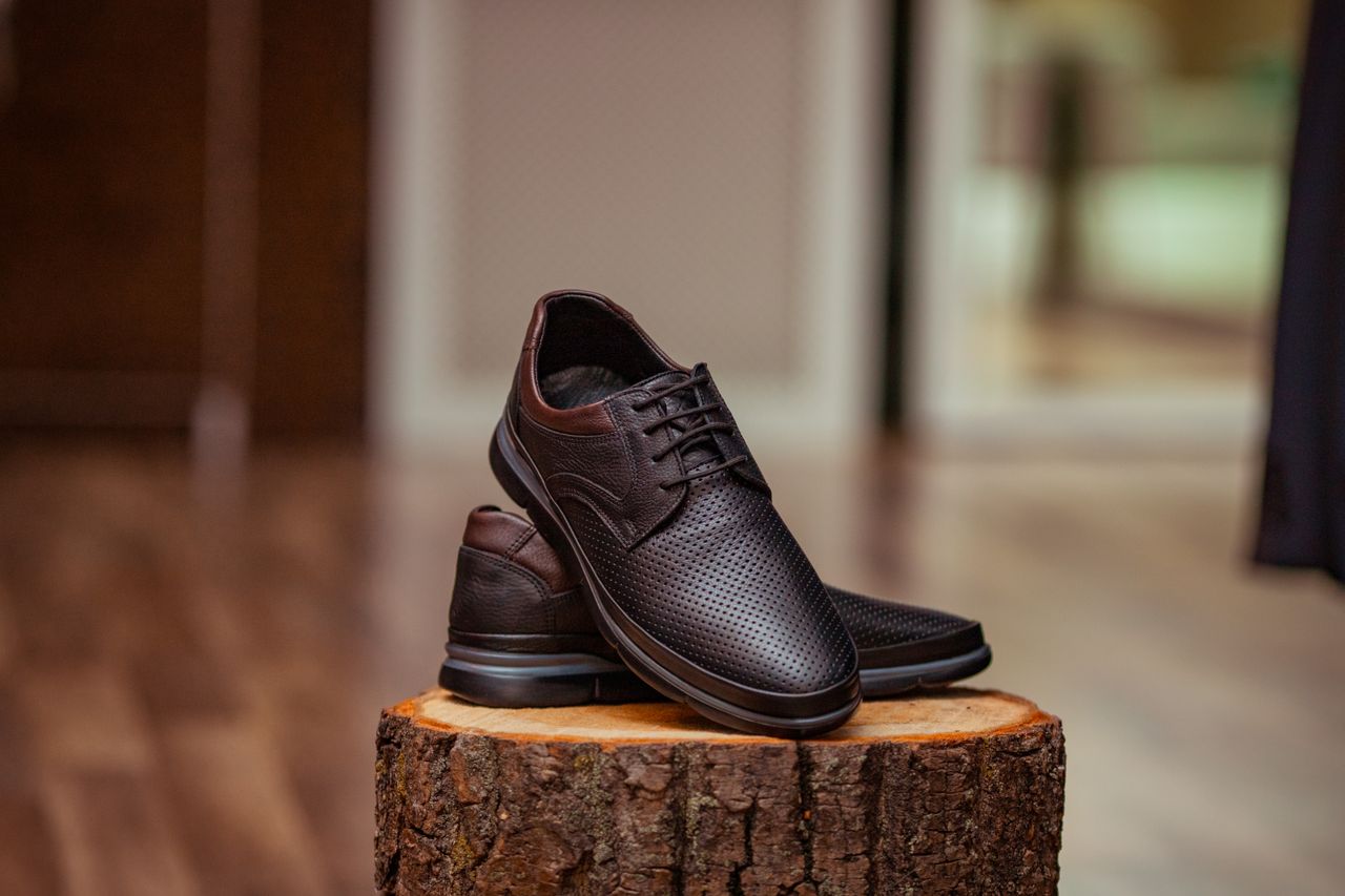 home-hero Stylish perforated leather shoes displayed elegantly on a rustic wooden stump indoors.